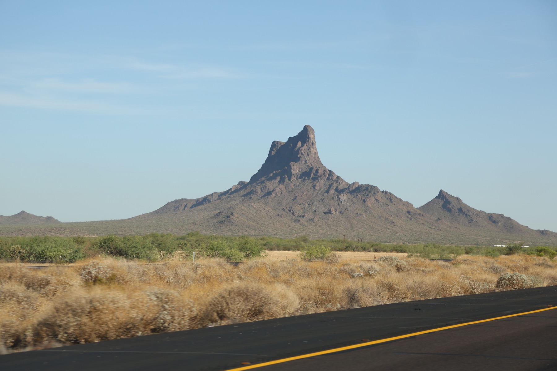 A desert highway approaching a rugged Southwestern peak